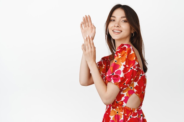 Portrait of feminine brunette girl dancing flamenco in floral dress clapping hands and smiling posing against white background