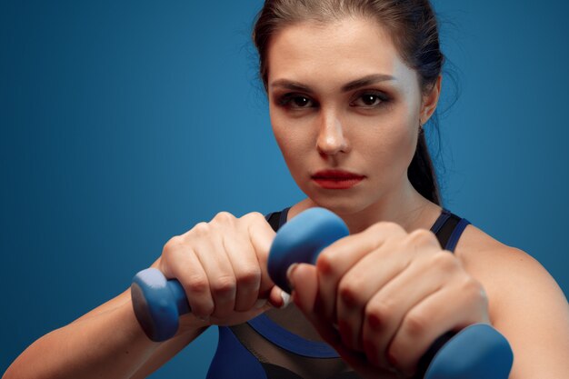 Photo portrait of a fitness model working out with dumbbells on grey