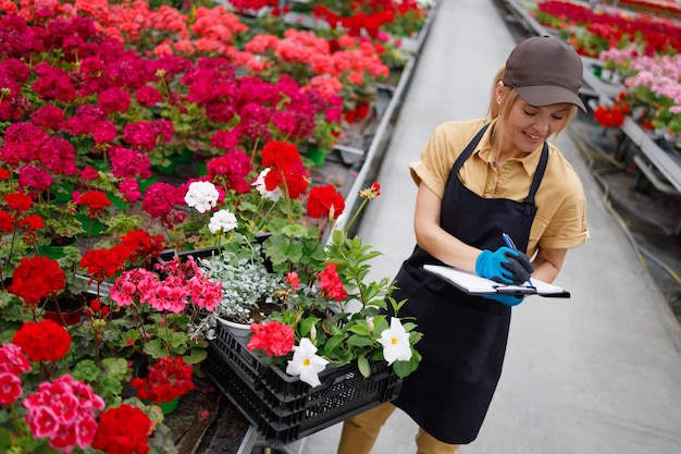 Portrait of florist woman at greenhouse in uniform and clipboard in her hand