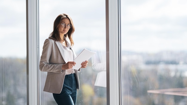 Portrait of focused business lady with documents standing near panoramic windows