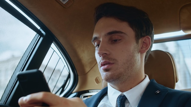 Portrait of focused business man writing message on phone in luxury automobile