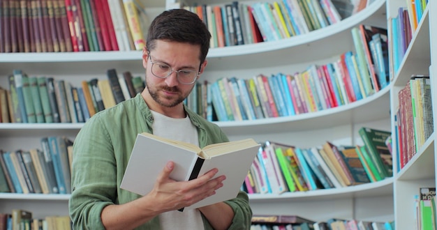 Portrait of focused man in glasses reading book from bookshelf for his class assignment and exam preparations University library concept