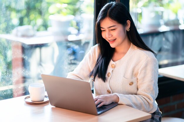 Portrait freelance business beautiful positive smile young asian woman online working with laptop computer at home in the living room indoors or the cafeBusiness Lifestyle