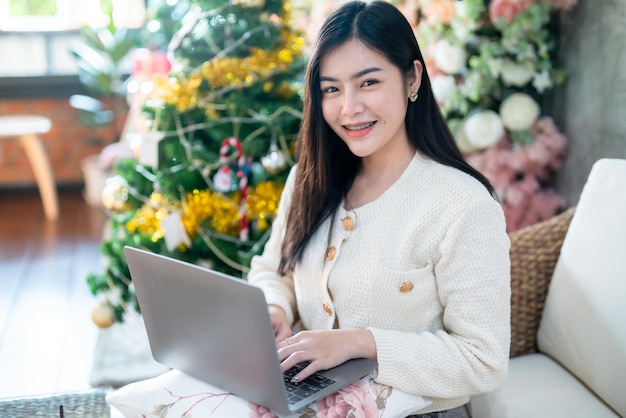 Portrait freelance business beautiful positive smile young asian woman online working with laptop computer at home in the living room indoors Decoration During Christmas xmas and New Year holidays