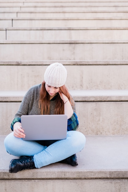 Portrait of freelancer woman using laptop while sitting on stairs in city street Blogger concept