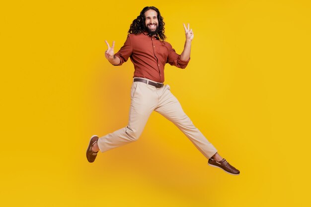 Portrait of friendly cheerful positive guy jump show v-signs on yellow background