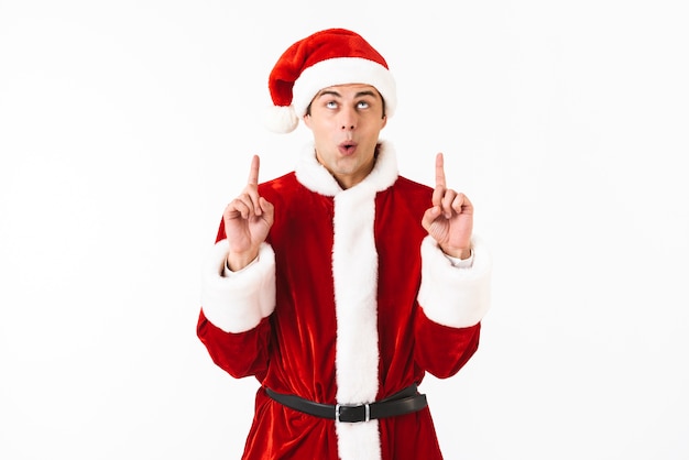 Portrait of friendly man 30s in santa claus costume and red hat gesturing fingers upward