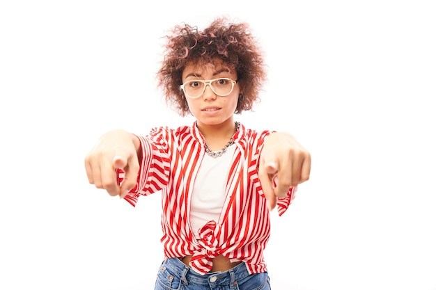 Portrait of friendly positive curly girl chooses you points finger at the camera isolated on white background