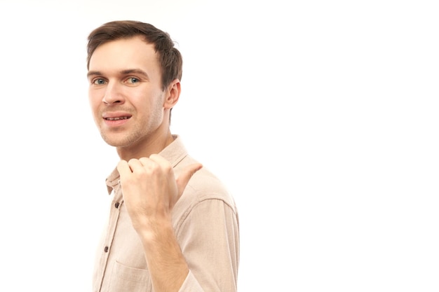 Portrait of friendly positive young man smiling pointing finger at empty copy space for text or product isolated on white background advertising banner