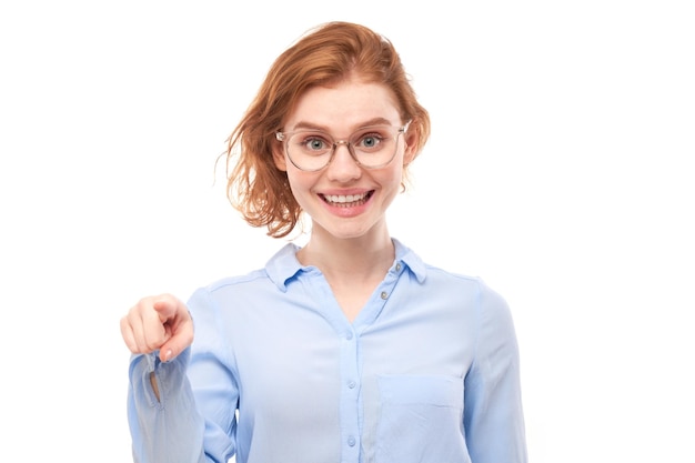 Portrait of friendly redhead girl chooses you points finger at the camera isolated on white background