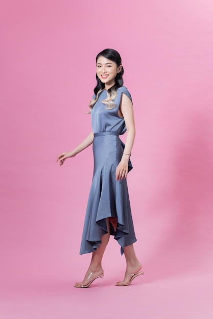 Portrait in full growth the young beautiful woman in a blue dress isolated on pink background