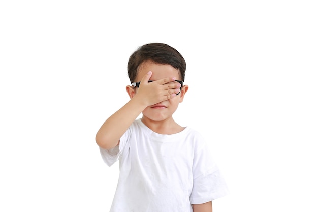 Portrait of funny Asian little boy child wearing glasses and closing hid eyes by one hand isolated over white background