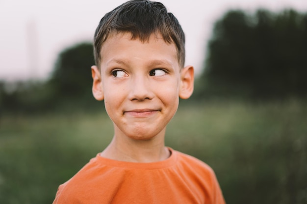 Portrait of a funny boy in a orange Tshirt and playing outdoors on the field at sunset Happy child lifestyle