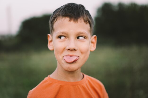 Portrait of a funny boy in a orange Tshirt and playing outdoors on the field at sunset Happy child lifestyle