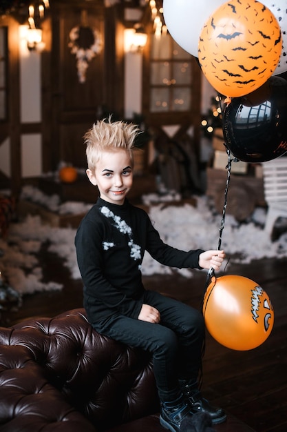 Portrait of a funny little boy in a skeleton costume holding a black balloon Happy Halloween