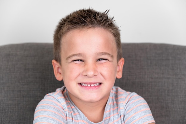 Portrait of a Funny little boy smiling and laughing looking at camera sitting on the couch at home Concept of a happy childhood