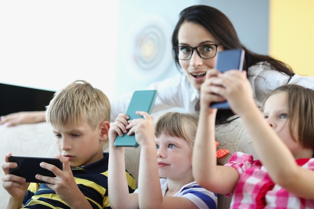 Portrait of funny mother watching over kids concentrated children holding smartphones and