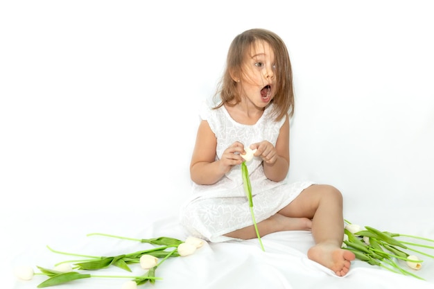 Portrait of a funny surprised little girl among white tulips on a white monochrome background