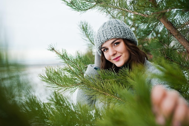 Portrait of gentle girl in gray coat and hat against new year tree outdoor