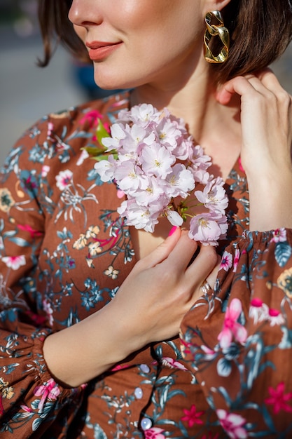 Portrait of a gentle woman against the background of sakura flowers. Walk in the blossoming sakura garden. Young stylish woman standing in sakura park and enjoying beauty