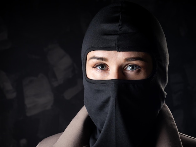 Portrait of a girl in a black balaclava and beige coat Shot in the studio on a dark background