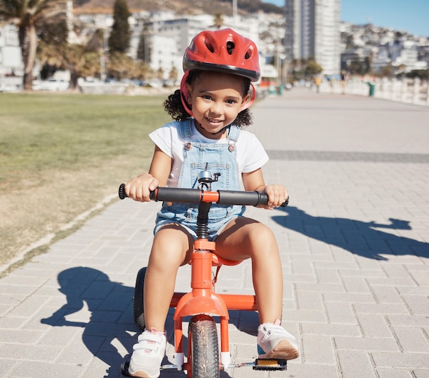 Portrait girl child and cycling on sidewalk learning to ride bike or healthy childhood development Happy kid riding tricycle with helmet safety and outdoor fun in summer sunshine and Atlanta USA