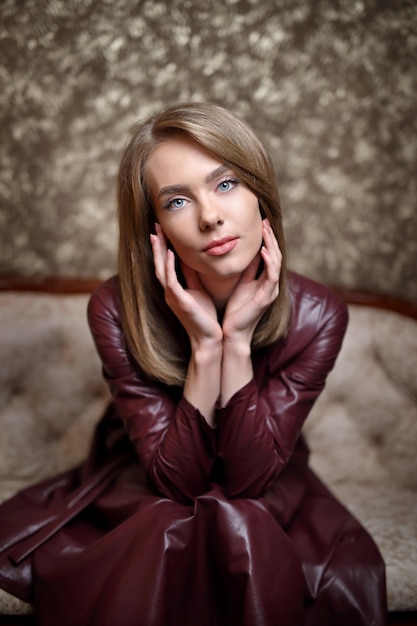 Portrait of a girl in a dark purple dress. Beautiful in a romantic mood, the girl looks at the camera, hands at the face, on a mottled brown background.