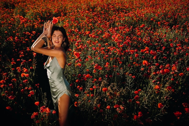 Portrait of a girl in a dress on a poppy field at sunset