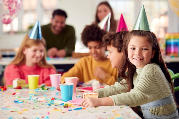 Portrait Of Girl Eating Birthday Cake At Party With Parents And Friends At Home