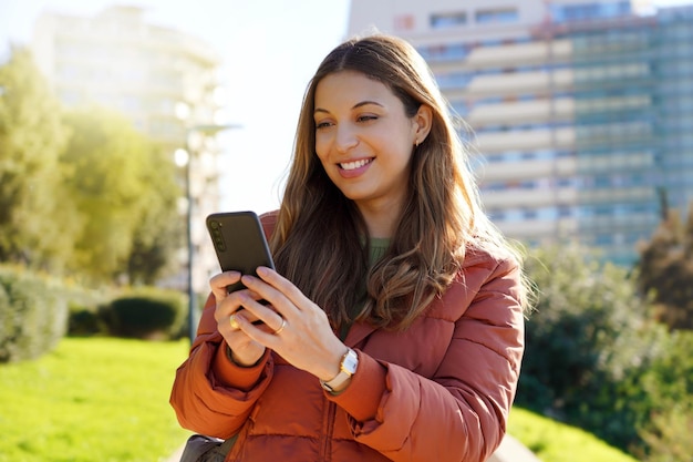 Portrait of girl outdoor using smartphone wearing winter coat watching video streaming