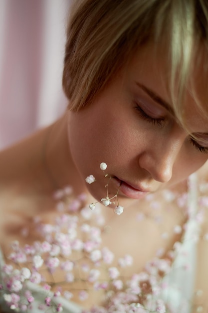 Portrait of a girl on a pink background with flowers Tenderness and feminine The sphere of beauty and women's health Short haircut blonde hair