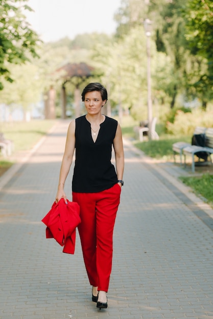 Portrait of a girl in a red suit standing in the alley of the park.