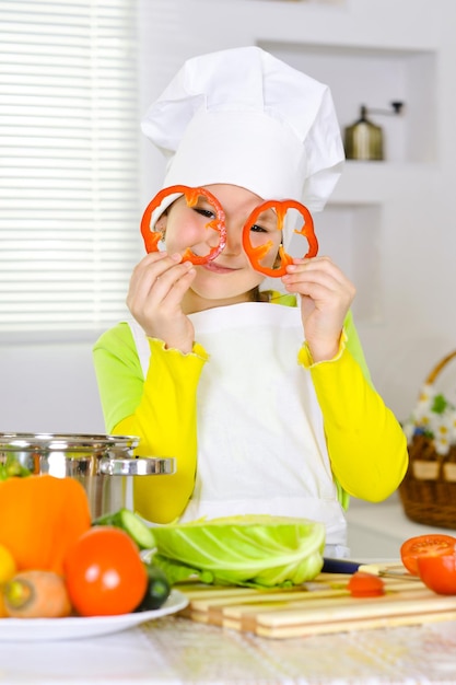 Portrait of girl wearing chef uniform holding slices of pepper