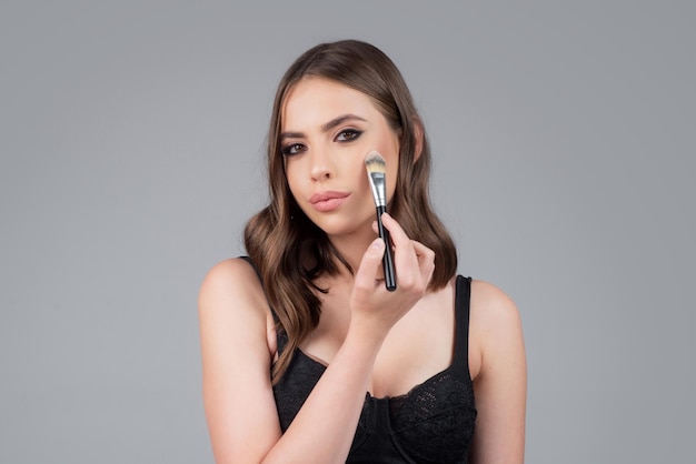 Portrait of a girl with cosmetic brush near face Woman holds makeup brush Closeup beauty portrait of attrctive cute sensual young woman Girl hold blush blusher apply powder