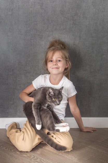 Portrait of a girl with a gray cat with yellow eyes in her hands on a gray background Vertical photo