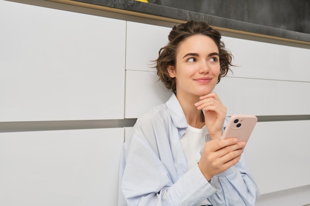 Portrait of girl with mobile phone sits on floor at home orders takeaway in app young woman with sma