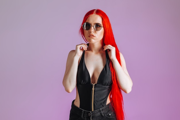 Portrait of a girl with red long hair in round glasses on a pink background