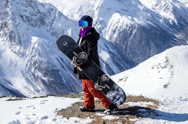 Portrait of a girl with snowboard on top of a snowy mountain.