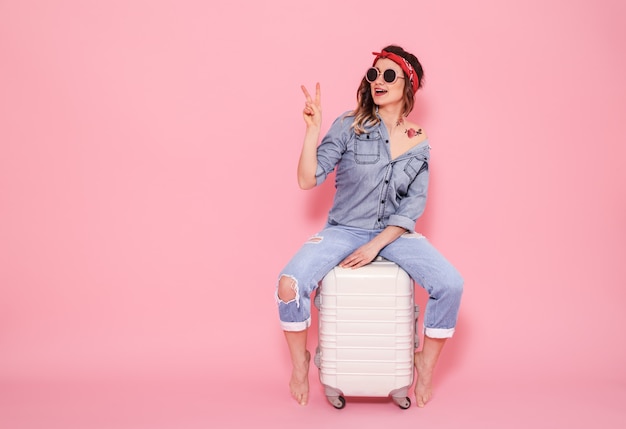 Portrait of a girl with a suitcase on a pink wall