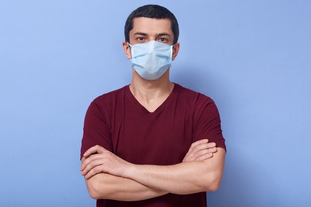 Portrait of good looking obedient man looking directly at camera, having folded arms, wearing antibacterial mask, protecting from coronavirus.