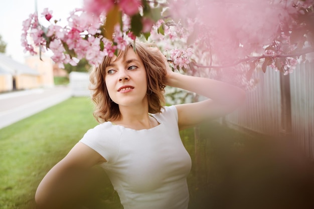 Portrait of goodlooking woman among pink bokeh flowers outdoors in spring selective focus