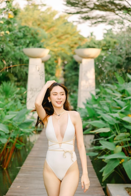 Portrait of gorgeous Asian woman model beauty skincare suntan walking in the tropical garden in white one piece swimsuit relaxing at beach summer resort Spa wellness laser