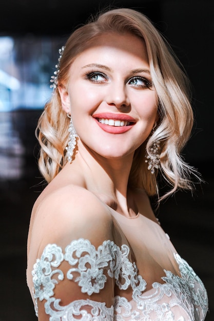 Portrait of gorgeous caucasian woman with wedding makeup and hairstyle posing in hotel room wearing elegant white dress