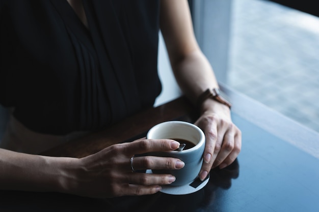 Portrait of gorgeous female drinking tea or coffee and looking with smile out of the coffee shop window while enjoying her leisure time, nice business woman lunch in modern cafe during her work break.