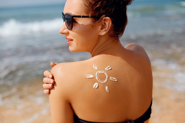 Portrait of gorgeous woman in bikini with the drawn sun on a shoulder at beach