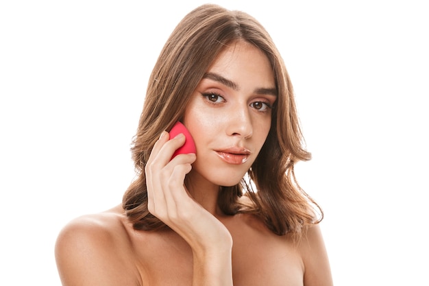 Portrait of gorgeous young half-naked woman applying makeup with sponge 