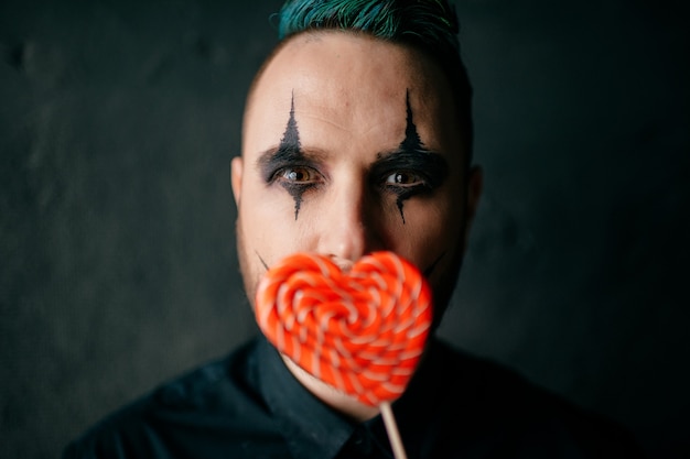 A portrait of gothic black clown posing with lollipop