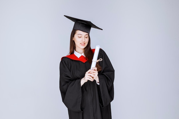 Portrait of graduate student in gown showing college certificate. High quality photo