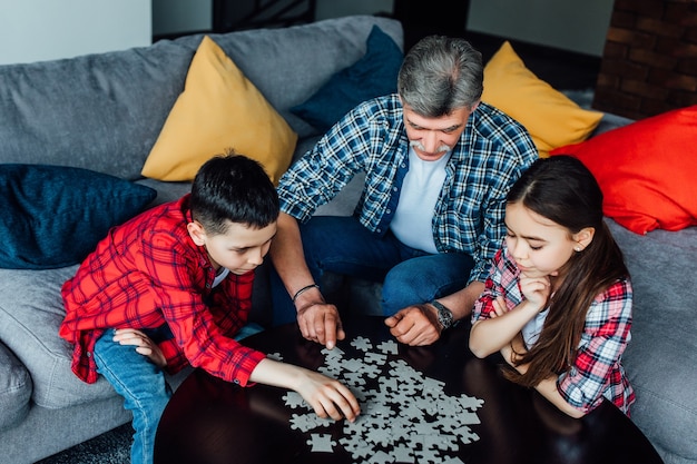 Portrait of grandfather and grandchild playing at home. Man and kid assembling Jigsaw Puzzle.