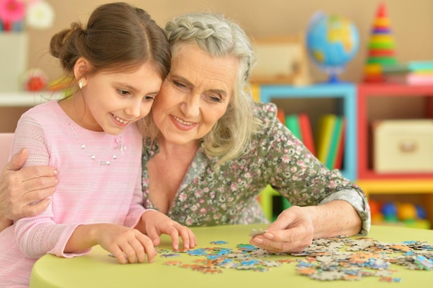 Portrait of grandmother collecting puzzle with her granddaughter